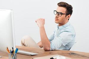 concentrato uomo d'affari. pensieroso giovane bello uomo guardare a il suo computer schermo mentre seduta a il suo Lavorando posto foto