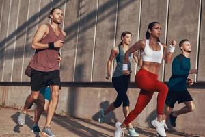 pieno lunghezza di persone nel gli sport capi di abbigliamento jogging mentre esercizio su il marciapiede all'aperto foto