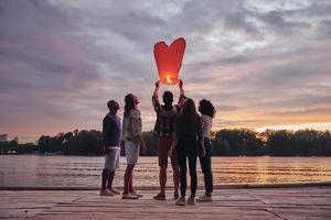 volante lontano... pieno lunghezza di giovane persone nel casuale indossare lasciare partire cielo lanterna mentre in piedi su il molo foto