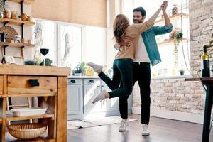 romanza. pieno lunghezza di bellissimo giovane coppia nel casuale capi di abbigliamento danza e sorridente mentre in piedi nel il cucina a casa foto