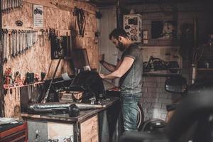 Lavorando nel riparazione negozio. fiducioso giovane uomo utilizzando opera attrezzo mentre Lavorando nel riparazione negozio foto