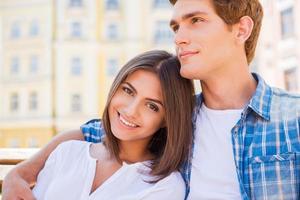 godendo loro tempo insieme. bellissimo giovane amorevole coppia seduta su il panchina insieme mentre donna guardare a telecamera e sorridente foto