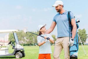 godendo grande gioco insieme. sorridente giovane uomo e il suo figlio guardare a ogni altro mentre in piedi su il golf corso foto