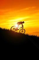 un' silhouette di un' ciclista discendente a partire dal il montagna nel il sera. foto