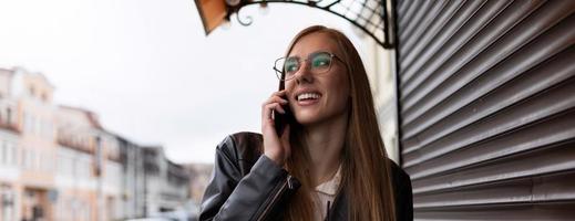 giovane snello ragazza chiamate su un' mobile Telefono con un' Sorridi su sua viso al di fuori il ufficio foto