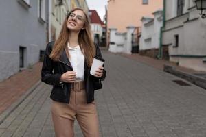 giovane donna turista passeggiate in giro il città con un' tazza di caffè nel sua mani e un' Telefono foto