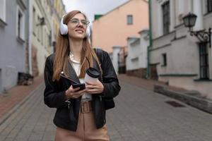 giovane donna turista nel cuffie con un' mobile Telefono passeggiate attraverso il vecchio città foto