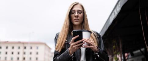 ritratto di un' grave giovane donna con un' tazza di caffè guardare a un' mobile Telefono foto