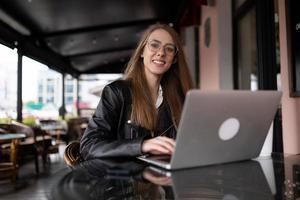 giovane elegante donna si siede su il le scale Il prossimo per un' popolare bar con un' tazza di caffè e orologi un' mobile Telefono foto