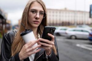 ritratto di un' grave giovane donna con un' tazza di caffè guardare a un' mobile Telefono foto