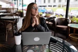 giovane femmina libero professionista Lavorando su un' il computer portatile nel un' città bar foto