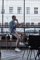 bene parlare con amico. bello giovane uomo parlando su il suo inteligente Telefono con Sorridi e Esprimere a gesti mentre seduta nel il caffetteria foto