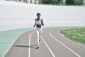 pieno lunghezza di bellissimo giovane africano donna nel gli sport capi di abbigliamento in esecuzione su traccia all'aperto foto