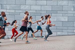 gruppo di giovane persone nel gli sport capi di abbigliamento jogging mentre esercizio su il marciapiede all'aperto foto