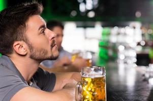 dopo il difficile Lavorando giorno. lato Visualizza di riflessivo giovane uomo potabile birra nel bar foto