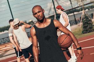 sensazione stanco. giovane africano uomo nel gli sport capi di abbigliamento guardare a telecamera mentre giocando pallacanestro all'aperto foto