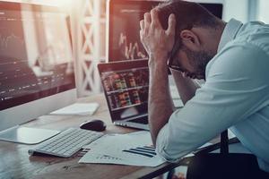 disastro frustrato giovane uomo d'affari nel vestito formale conservazione testa nel mani mentre seduta nel il ufficio foto