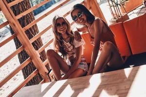 Questo estate è caldo superiore Visualizza di attraente giovane donne sorridente mentre seduta nel il spiaggia bar foto