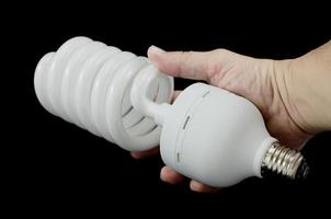 mano che tiene la lampadina a risparmio energetico, isolata su sfondo nero