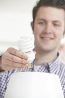 uomo che mette la lampadina a basso consumo energetico nella lampada a casa foto