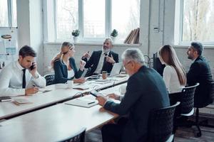 collaboratori nel elegante vestito formale utilizzando moderno tecnologie mentre Lavorando nel il ufficio foto