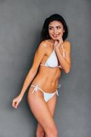 naturale e Bellissima. attraente giovane sorridente donna nel bianca bikini in posa contro grigio sfondo foto