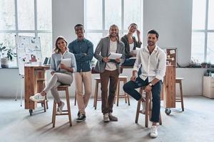 giovane attività commerciale professionisti. pieno lunghezza di giovane moderno persone nel inteligente casuale indossare sorridente e guardare a telecamera mentre in piedi nel il creativo ufficio foto