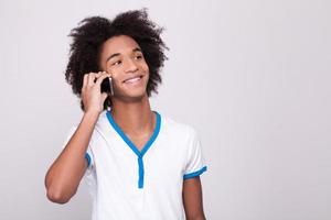 spensierato parlare. allegro africano adolescente Lavorando su digitale tavoletta e sorridente mentre in piedi isolato su grigio sfondo foto