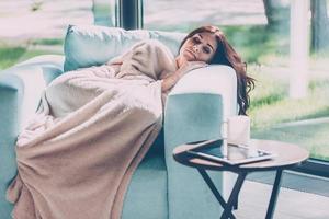 giorno sognando. bellissimo giovane donna addormentato nel un' grande confortevole sedia a casa mentre essere coperto con coperta foto