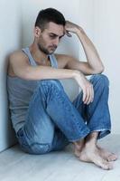 depresso e senza speranza. depresso giovane uomo seduta su il pavimento e Tenere testa nel mano foto