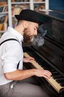 lui avuto il suo proprio tecnica. profilo di bello giovane barbuto uomini giocando pianoforte e fumo sigaretta foto
