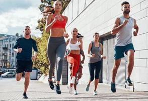pieno lunghezza di persone nel gli sport capi di abbigliamento jogging mentre esercizio su il marciapiede all'aperto foto