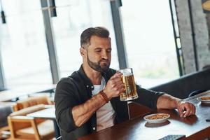 bello giovane uomo nel casuale capi di abbigliamento godendo birra mentre la spesa tempo nel il pub foto