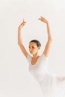 danza con passione. bellissimo giovane ballerina nel bianca tutu conservazione braccia sollevato mentre danza contro bianca sfondo foto