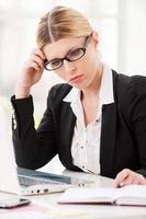 pensiero di soluzioni. riflessivo maturo donna nel vestito formale Tenere testa nel mano mentre seduta a sua Lavorando posto foto