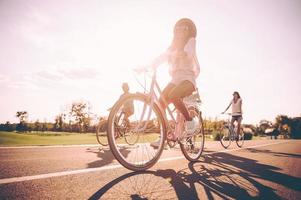 Ciclismo con divertimento. Basso angolo Visualizza di giovane persone equitazione biciclette lungo un' strada e guardare contento foto