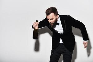 pure molti bolle. bello giovane uomo nel pieno completo da uomo potabile Champagne a partire dal il bottiglia mentre in piedi contro grigio sfondo foto