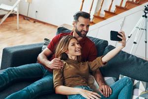 carino giovane coppia nel casuale capi di abbigliamento bonding insieme e sorridente mentre assunzione autoscatto in casa foto