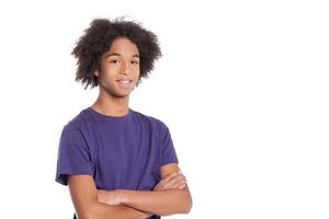 fiducioso adolescente. sorridente africano adolescenziale ragazzo conservazione braccia attraversato e sorridente mentre in piedi isolato su bianca foto