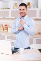 mattina vestito su. contento giovane uomo regolazione maniche su il suo camicia e guardare a telecamera mentre in piedi nel il cucina foto