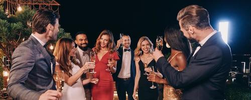 gruppo di bellissimo persone nel vestito formale comunicare e sorridente mentre la spesa tempo su lusso festa foto