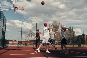 tiro a obiettivo. gruppo di giovane uomini nel gli sport capi di abbigliamento giocando pallacanestro mentre la spesa tempo all'aperto foto