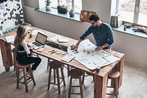 sviluppando nuovo strategia. superiore Visualizza di giovane colleghi nel inteligente casuale indossare utilizzando planimetria mentre Lavorando nel il creativo Lavorando spazio foto