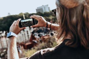 condivisione il Visualizza. posteriore Visualizza di giovane uomo Fotografare il Visualizza utilizzando inteligente Telefono mentre in piedi su il collina all'aperto foto