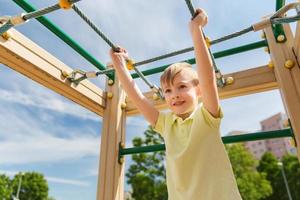 ragazzino felice arrampicata sul parco giochi per bambini foto