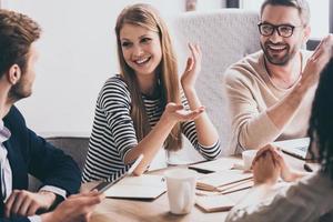 condivisione il ultimo notizia. allegro giovane persone guardare a ogni altro con Sorridi mentre seduta a il ufficio tavolo a il attività commerciale incontro foto