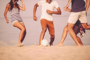 spiaggia palla con gli amici. ritagliata Immagine di giovane persone giocando con calcio palla su il spiaggia foto