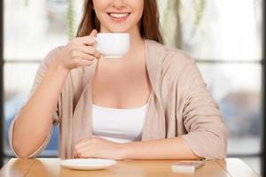 potabile un' fresco caffè. ritagliata Immagine di bellissimo giovane donna potabile caffè a il ristorante e sorridente a telecamera foto