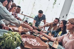 grande cibo e azienda. gruppo di giovane persone nel casuale indossare mangiare e sorridente mentre avendo un' cena festa foto