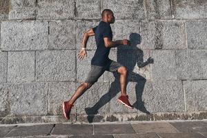 spingendo per il limite. pieno lunghezza di giovane africano uomo nel gli sport capi di abbigliamento jogging mentre esercizio all'aperto foto